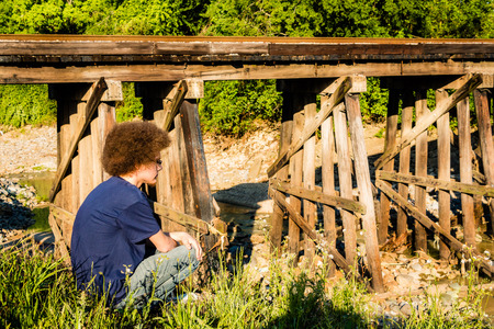 Young man crouching with railroad bridge in backgroundの写真素材