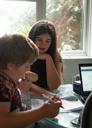 Two school age children, 13 and 8 helping each other with their homeworkの写真素材