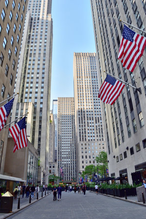 New York, USA - May 15 2023: A city street with a large number of people walking down it. The street is lined with tall buildings and a flag pole with American flagsのeditorial素材