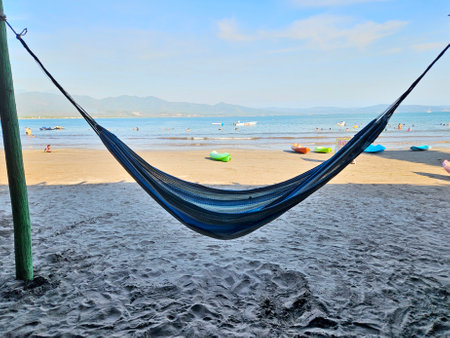 A blue and white hammock is hanging over Islitas beach in Nayarit. The beach is crowded with people and there are several boats in the waterの写真素材