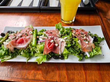 A plate of a salad with a glass of orange juice on a table. The plate has three pieces of food on it, and the orange juice is in a glass. Scene is casual and relaxedの写真素材