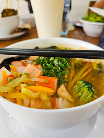 Vertical close-up of delicious Asian noodle soup. Includes vibrant crab sticks, fresh broccoli,...