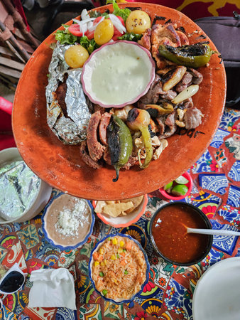 Mexican parrillada platter with grilled meats, roasted vegetables, and salad. Sides of beans, rice, and salsa on a colorful Tlaquepaque table.の写真素材