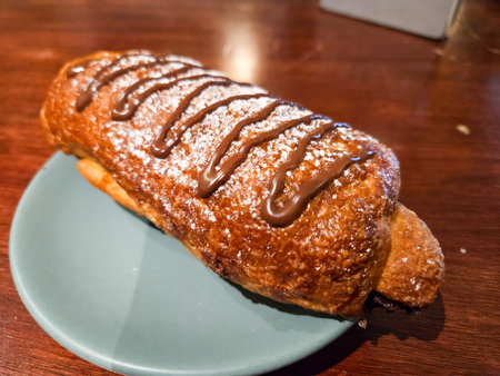 Golden-brown sweet bread, generously topped with chocolate drizzle and powdered sugar. Served on a blue plate, ready to be enjoyedの写真素材