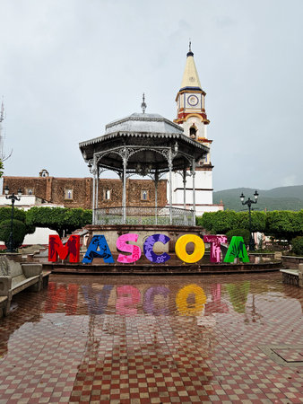 Mascota, Mexico - July 16 2024: Vibrant Mascota town sign, classic gazebo, and church in Jalisco, Mexico. Wet pavement reflects colorful letters, capturing town charm.のeditorial素材