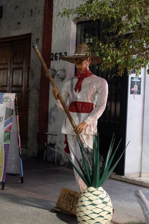 Tlaquepaque, Mexico - April 19 2025: Sculpture of a jimador holding a stick next to an agave pina, wearing folk clothes and sombreroのeditorial素材