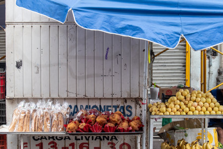 Guadalajara, Mexico - August 30 2025: Vibrant market stall with fresh guavas, bananas, and traditional baked goods under a blue canopy. Captures authentic local urban commerceのeditorial素材