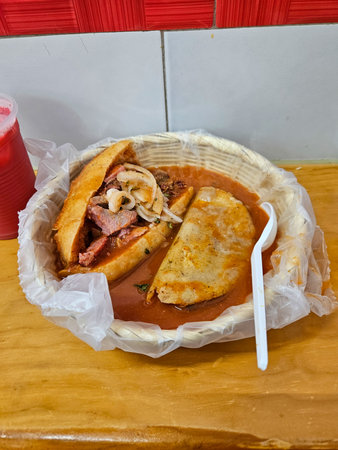 Traditional Mexican Torta Ahogada and a savory quesadilla submerged in vibrant spicy red chili sauce in a rustic basketの写真素材