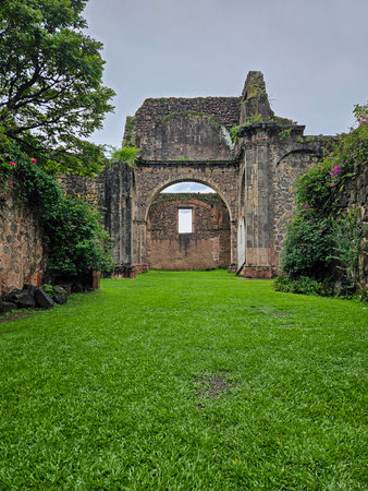 Ancient Unfinished Temple of Precious Blood ruins. Stone archway, weathered walls, lush green grass, overcast sky. Evokes history and natural beauty. Serene.のeditorial素材