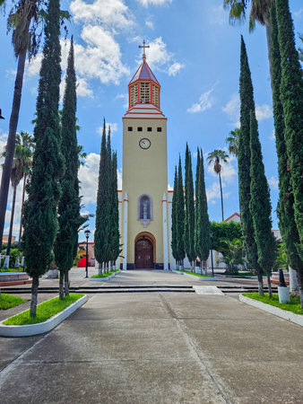 Ayutla, Mexico - July 16 2024: Saint Michael Archangel church, Ayutla, Jalisco. Bell tower, clock, and cypress trees. Sunny blue sky.のeditorial素材