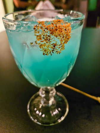 A vibrant blue margarita cocktail, served in a classic glass with ice, adorned with a distinctive chili lime spice garnish, captured in a dimly lit bar settingの写真素材