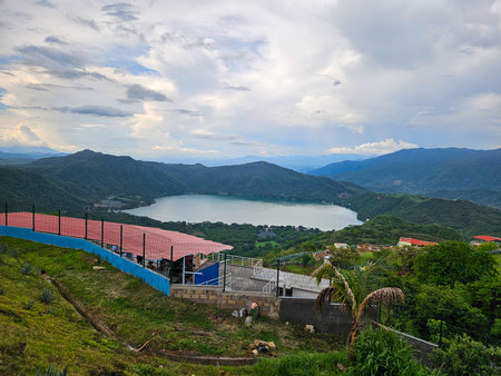 Panoramic view of Santa Maria del Oro Lagoon, a vibrant caldera lake in Nayarit, Mexico. Surrounded by lush green mountains under a cloudy sky.の写真素材