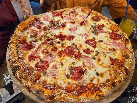 Appetizing pizza with varied meat toppings and melted cheese. Features a unique sesame seed crust, served on a wooden board, ideal for sharingの写真素材
