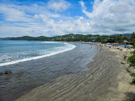 Lively Sayulita Beach, Nayarit, Mexico. People swimming and relaxing with colorful umbrellas, boats, and lush hills on the vibrant Pacific coastの写真素材