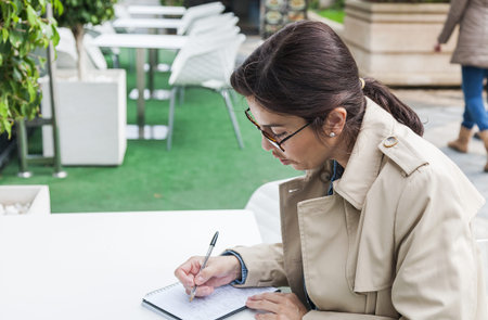 Brunette woman working outside with phone and tablet, drinking coffee