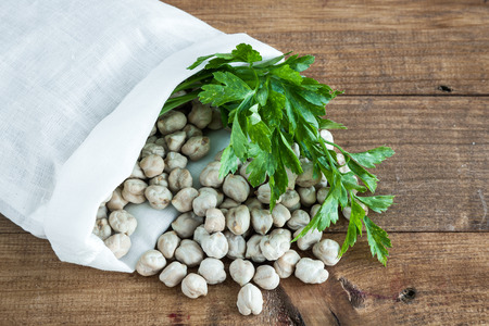 Sack with chickpeas and parsley on wooden tableの写真素材