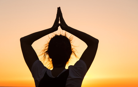 Silhouette young woman practicing yoga on the mediterranean beach at sunset.の写真素材