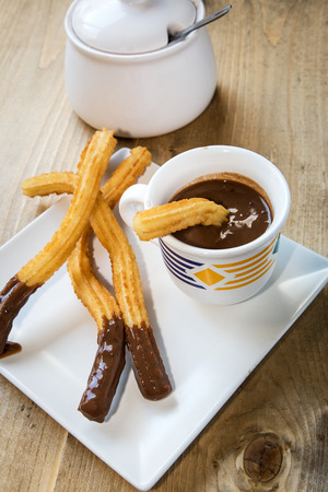 Churros with hot chocolate and sugar on old wooden tableの写真素材