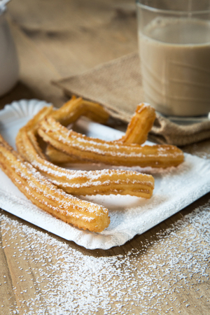Churros with coffee with milk and sugar on old wooden tableの写真素材
