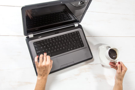 Woman at laptop with coffee cup on white wooden table