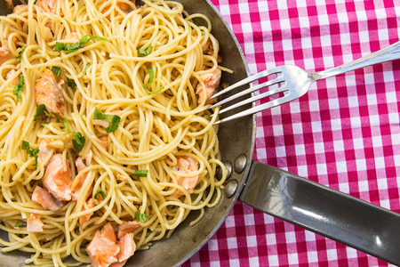 Noodles with salmon and parsley in pan on checkered tableclothの写真素材
