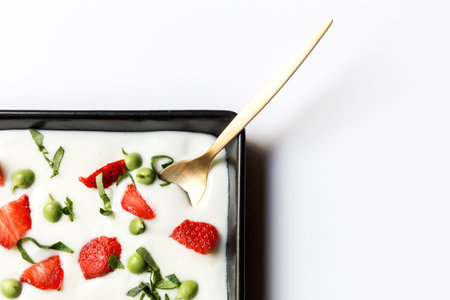 Close-up of black plate with green peas and sliced strawberry in cream. Isolated, from above