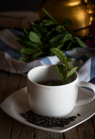 Close-up of vintage metal kettle with glass of herbal tea on kitchen towel on tableの写真素材