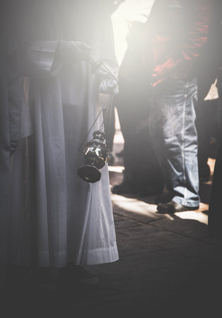 Priest in white clothes holding smoking thurible in close-up