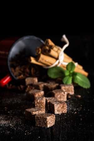 Lumps of brown sugar on black wooden table with cinnamon and anise starsの写真素材