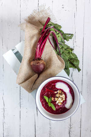beet soup in a white bowl on wooden surface - healthy food