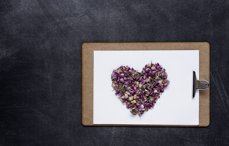 Clipboard with a blank sheet of paper on light and a heart of flowers on black background with plenty of copy space. Valentine's Dayの写真素材