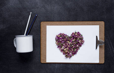 Clipboard with a blank sheet of paper on light and a heart of flowers on black background with...