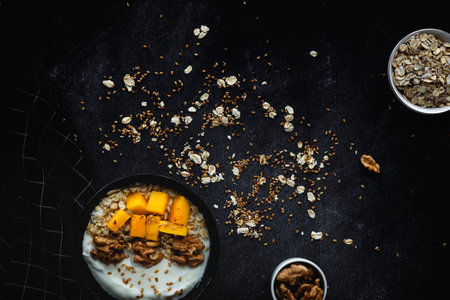Bowl of homemade granola with yogurt and cereals and mango fruit and walnuts on dark background from top view. Healthy food From above. Flat layの写真素材