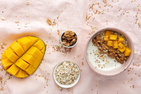 Bowl of homemade granola with yogurt and cereals and mango fruit and walnuts on pink background from...
