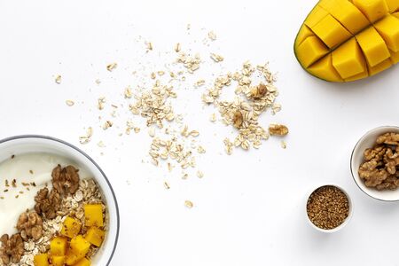 Bowl of homemade granola with yogurt and cereals and mango fruit and walnuts on white background from top view. Healthy food From above. Flat layの写真素材
