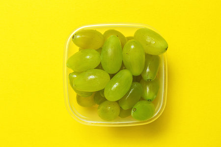Fresh seasonal grapes in Plastic containers ready to eat To take away. On yellow background. Healthy...