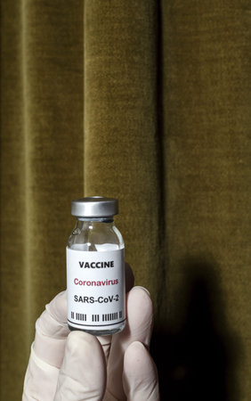 Covid-19 vaccine with syringe in hands of unrecognizable doctor under high contrast light