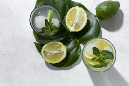 Refreshing homemade glass lemonade with ice and mint in sunlight on white background