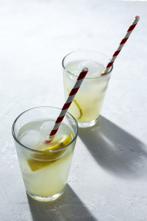 Refreshing homemade glass lemonade with ice and mint in sunlight on white backgroundの写真素材