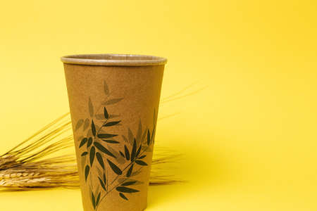 disposable glass with ear of wheat on yellow background. Caring for the environment. The problem is recycling. Reuse. Place for text.の写真素材