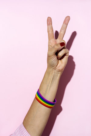 Woman hands with LGBT bracelet on pink background