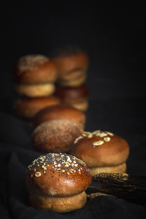 Assorted round homemade brioche buns with seeds on dark background with high contrast light. Isolatedの写真素材