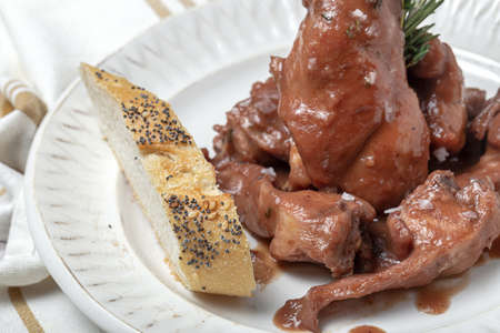 Traditional homemade rabbit meat stew with red wine sauce with aromatic herbs on a marble backgroundの写真素材