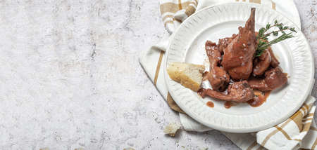 Traditional homemade rabbit meat stew with red wine sauce with aromatic herbs on a marble backgroundの写真素材