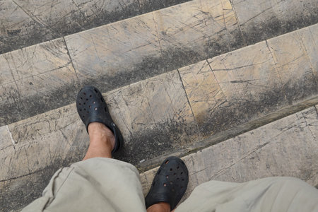 Person descending worn, scratched stone steps wearing black sandals and light-colored shorts.