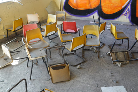 An abandoned classroom filled with dusty, colorful chairs, some overturned, with graffiti-covered walls in the background.の写真素材