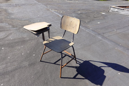 A single old school desk with rusted legs and a wooden seat, standing alone on an empty rooftop...
