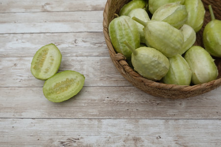 Fresh maroon cucumbers in a woven basket with two halves showing the seeds on a rustic wooden surface.の写真素材