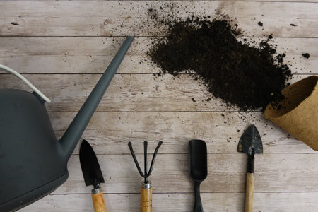Gardening tools, watering can, and soil spilling from a pot create a scene of springtime planting preparationの写真素材
