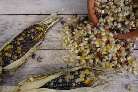 Colorful glass gem corn kernels spilling from a terracotta bowl onto a wooden table with two...
